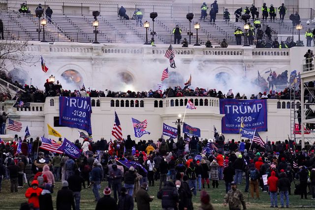 Hundreds of protesters on the plaza outside hte US Capitol, climbing the walls, with smoke